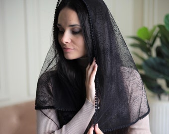 May include: A black sheer veil with a dotted pattern and a black beaded trim. The veil is draped over a person's head and shoulders.