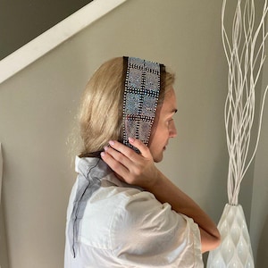 May include: A decorative headband with a grid pattern of iridescent rhinestones. The headband is dark brown with a sheer black fabric on the sides. The person is wearing a white button-down shirt.