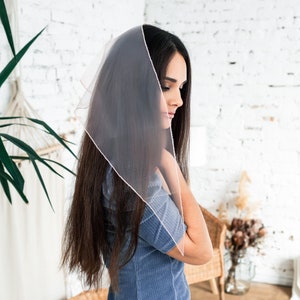 May include: A woman with long dark hair wearing a sheer pink scarf over her head and a blue corduroy dress.