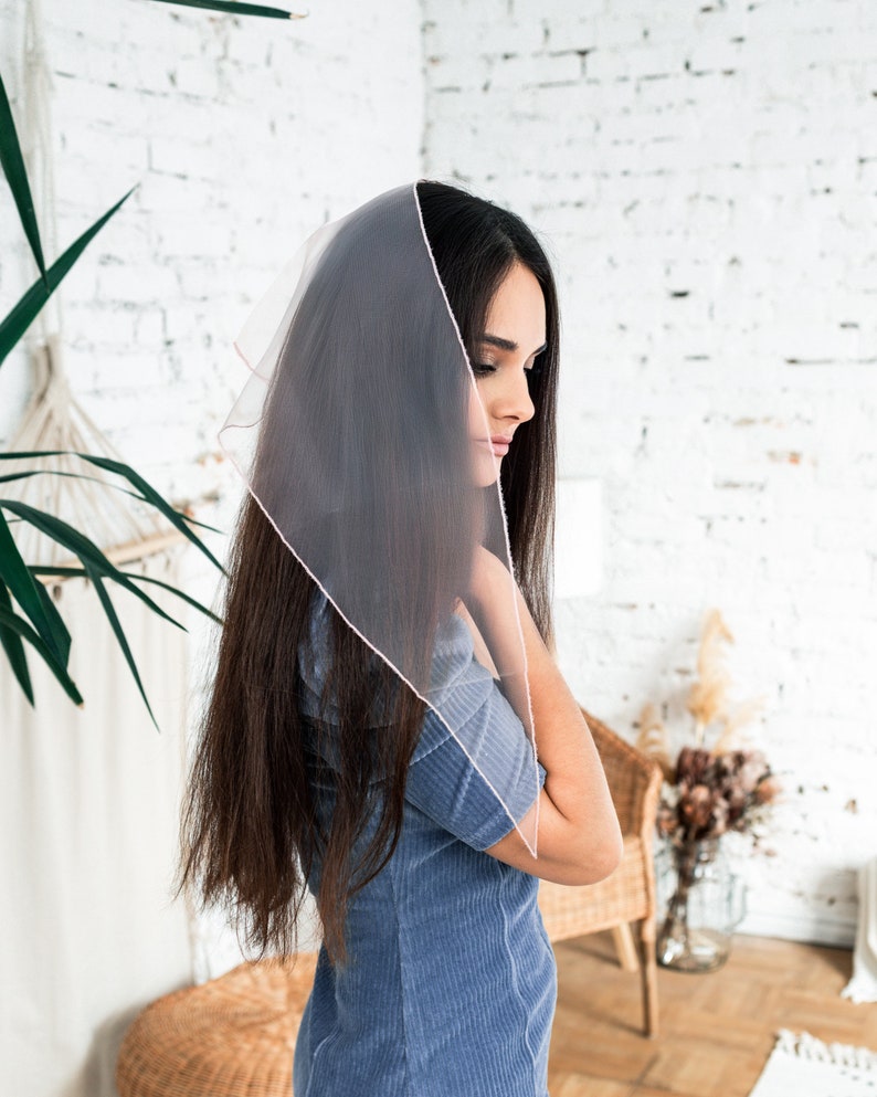 May include: A woman with long dark hair wearing a sheer pink scarf over her head and a blue corduroy dress.