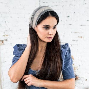 Pu&ograve; includere: Una donna con lunghi capelli scuri indossa un vestito blu chiaro con una cerniera sul davanti. Indossa una fascia leggera di colore grigio chiaro.