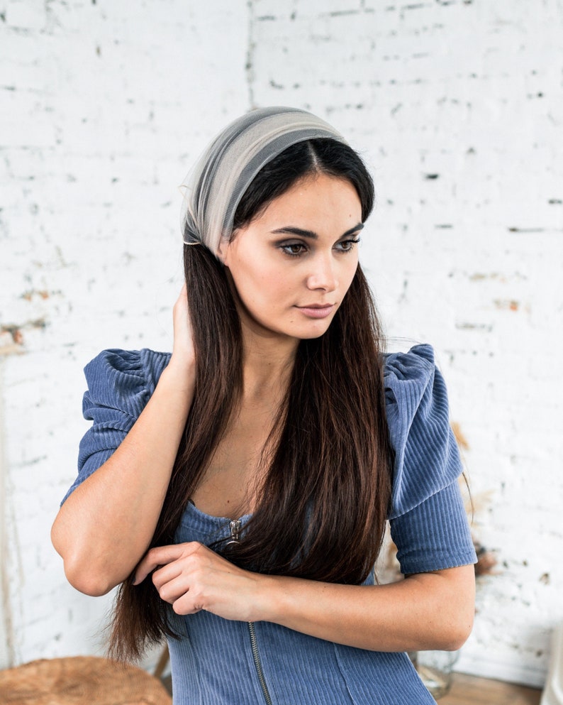 Pu&ograve; includere: Una donna con lunghi capelli scuri indossa un vestito blu chiaro con una cerniera sul davanti. Indossa una fascia leggera di colore grigio chiaro.