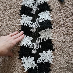 May include: Black and white floral lace applique with a black satin ribbon. The applique features a repeating pattern of white flowers on a black background, with a delicate net-like design.