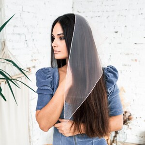 May include: A woman with long dark hair wearing a blue corduroy dress with a sheer pink scarf draped over her head.