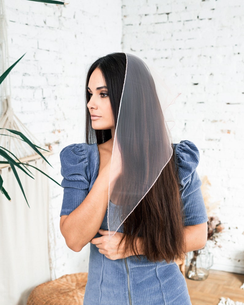 May include: A woman with long dark hair wearing a blue corduroy dress with a sheer pink scarf draped over her head.