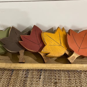May include: Five wooden fall leaves in a wooden bowl. The leaves are painted in shades of green, brown, red, yellow, and orange.