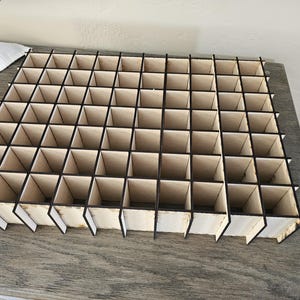 May include: A wooden organizer with 48 square compartments. The organizer is made of light brown wood with black trim.