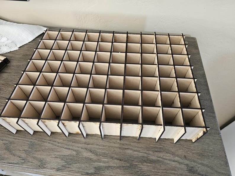May include: A wooden organizer with 48 square compartments. The organizer is made of light brown wood with black trim.
