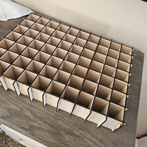 May include: A wooden organizer with a grid of compartments, perfect for storing small items. The organizer is made of light brown wood with black dividers.