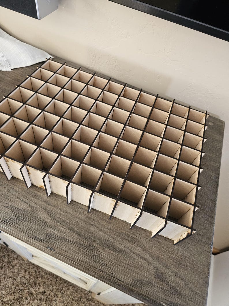 May include: A wooden organizer with a grid of compartments, perfect for storing small items. The organizer is made of light brown wood with black dividers.