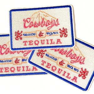 May include: Three white fabric patches with blue trim and red and pink embroidered text. The text reads "Cowboys Tequila" with the words "The Likkerd" and "Since 1973" in smaller font.