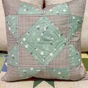 May include: A brown and green patchwork cushion with a star design. The cushion is made of gingham fabric and has a floral pattern.