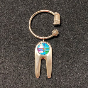 May include: A silver-toned golf ball marker and key ring. The marker has a colorful inlaid design with blue, green, purple, and orange hues. The key ring features a textured golf club head and a small, textured ball.