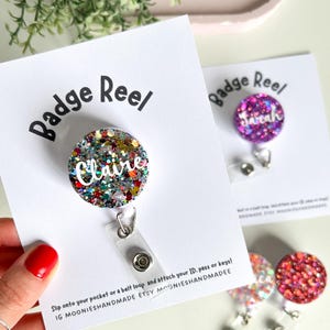 May include: Glitter badge reels with the names "Claire" and "Sarah". The reels are round and have a clear plastic strap with a snap closure. The text "Badge Reel" is printed on the white card.