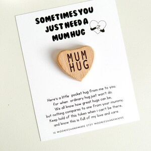 May include: A wooden heart-shaped token with the words "Mum Hug" engraved on it. The token is accompanied by a card with a message about the importance of hugs and the love and care they represent.