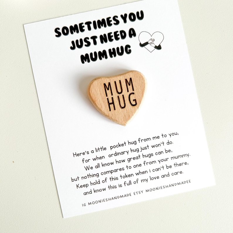May include: A wooden heart-shaped token with the words "Mum Hug" engraved on it. The token is accompanied by a card with a message about the importance of hugs and the love and care they represent.