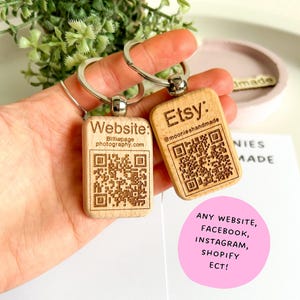 May include: Two wooden keychains with engraved QR codes and text. The keychain on the left says "Website: Billiepage photography.com". The keychain on the right says "Etsy: @moonieshandmade".