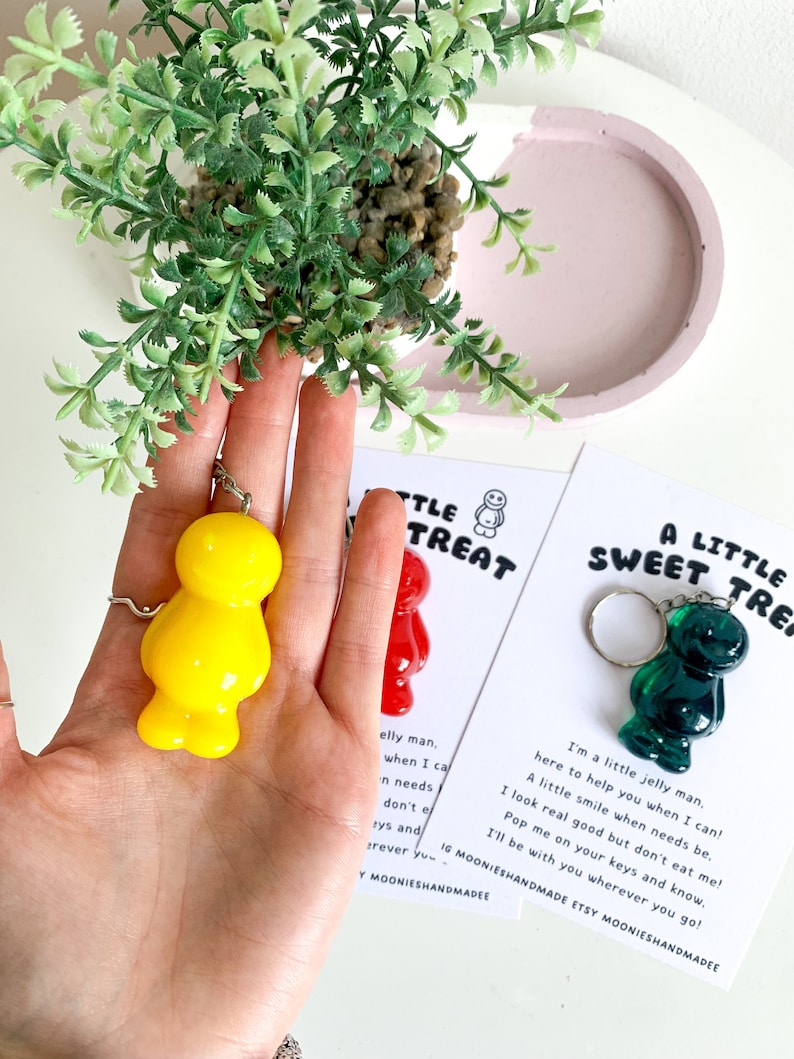 May include: Two keychains featuring a yellow and a green jelly bean shaped charm. The charms are attached to silver key rings. The keychains are displayed on cards with the text "A Little Sweet Treat" and "A Little Treat".