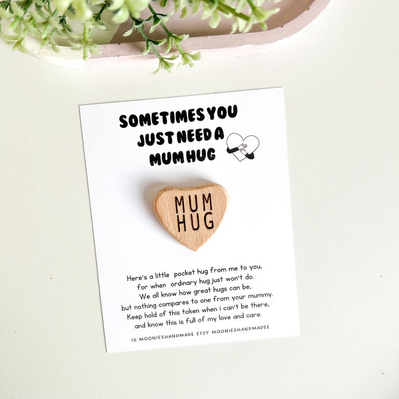 May include: A wooden heart-shaped token with the words "Mum Hug" engraved on it. The token is on a white card with the text "Sometimes you just need a Mum Hug" and a small illustration of two hands hugging.