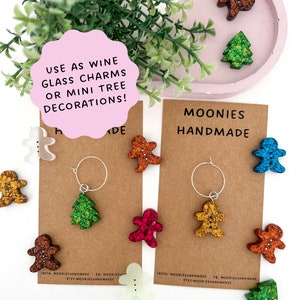 May include: An assortment of handmade Christmas decorations in various colours and designs, including gingerbread people, Christmas trees, and a white gingerbread person. The decorations are made of resin and have a glittery finish. The decorations are displayed on a brown card with the text "Moonies Handmade".