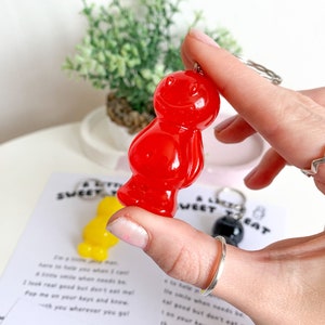 May include: A red gummy bear keychain with a silver key ring. The keychain is being held by a hand. The text "A Little Sweet Treat" is visible in the background.