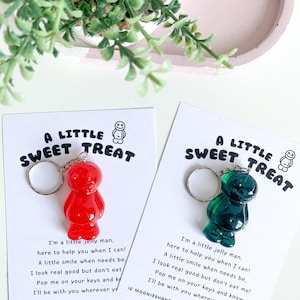May include: Two keychains featuring a red and a green jelly bean shaped charm. The charms are attached to a silver key ring. Each keychain has a card attached with a message that reads "A Little Sweet Treat" and a short poem about the jelly bean charm.