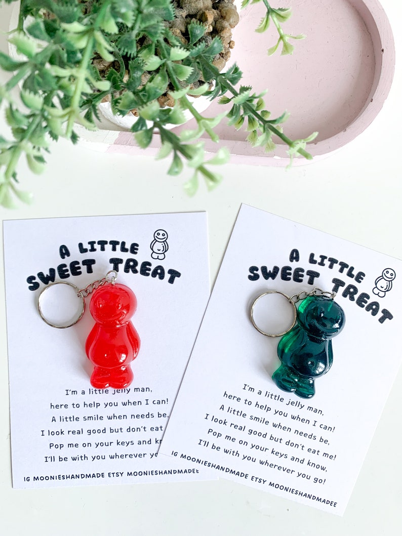May include: Two keychains featuring a red and a green jelly bean shaped charm. The charms are attached to a silver key ring. Each keychain has a card attached with a message that reads "A Little Sweet Treat" and a short poem about the jelly bean charm.