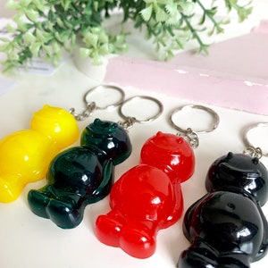 May include: Four gummy bear keychains in different colors: yellow, green, red, and black. Each keychain has a smiling face and is attached to a silver key ring.