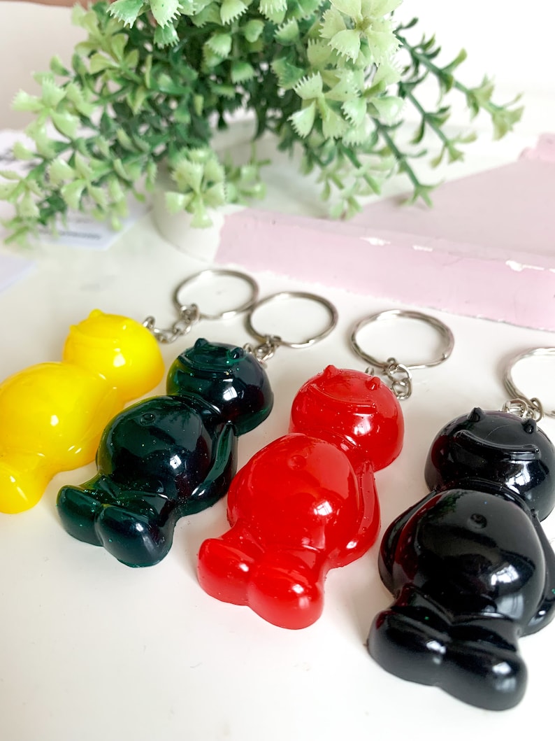 May include: Four gummy bear keychains in different colors: yellow, green, red, and black. Each keychain has a smiling face and is attached to a silver key ring.