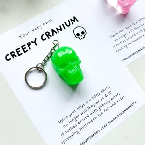 May include: A neon green skull keychain with a silver chain and keyring. The keychain is on a white card with the text "Your very own CREEPY CRANIUM" and a small skull graphic. The card also includes text about Halloween.