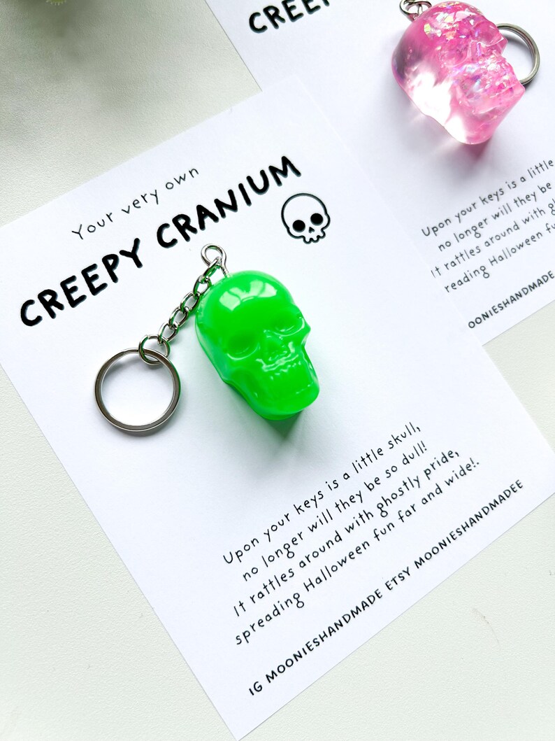 May include: A neon green skull keychain with a silver chain and keyring. The keychain is on a white card with the text "Your very own CREEPY CRANIUM" and a small skull graphic. The card also includes text about Halloween.