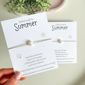 May include: A white string bracelet with a white seashell charm and a star charm. The bracelet comes with a card that reads "A little bracelet for Summer" and has a poem about summer days.