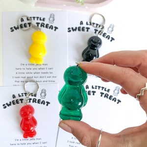 May include: Four jelly bean shaped keychains in different colors: red, yellow, green, and black. Each keychain has a small tag that reads "A Little Sweet Treat" and includes a short poem about the keychain.
