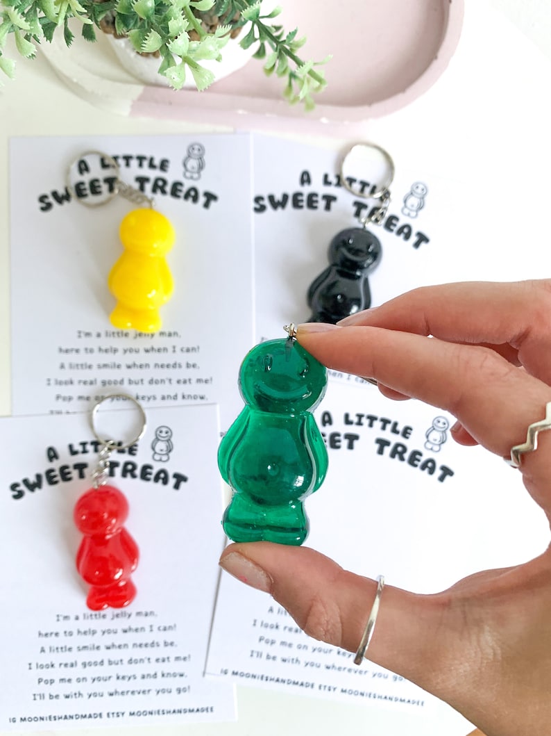 May include: Four jelly bean shaped keychains in different colors: red, yellow, green, and black. Each keychain has a small tag that reads "A Little Sweet Treat" and includes a short poem about the keychain.