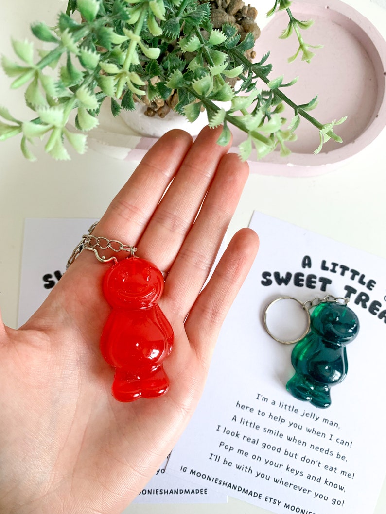 May include: A red and green jelly bean keychain with a silver chain. The keychain is accompanied by a card that reads "A Little Sweet Treat" and includes a short poem about the jelly bean.