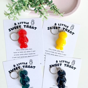 May include: Four keychains featuring a jelly bean character with a smiling face. The keychains are on cards with the text "A Little Sweet Treat" and a short poem about the jelly bean character. The jelly beans are red, yellow, green, and black.