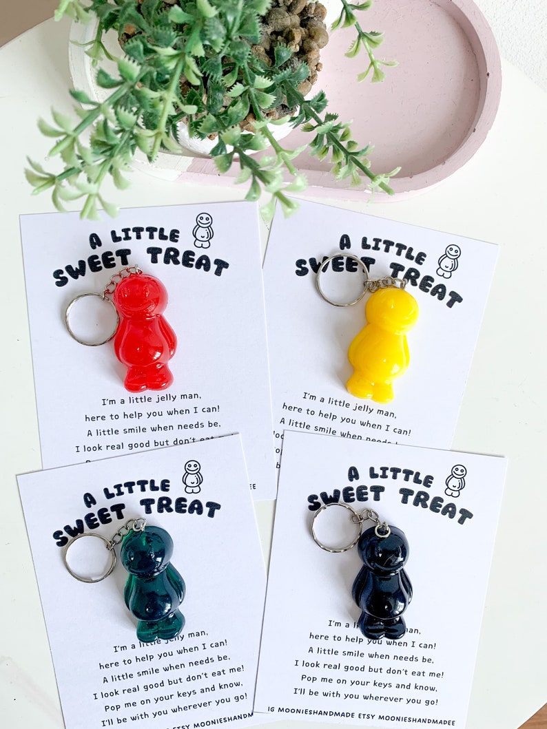 May include: Four keychains featuring a jelly bean character with a smiling face. The keychains are on cards with the text "A Little Sweet Treat" and a short poem about the jelly bean character. The jelly beans are red, yellow, green, and black.