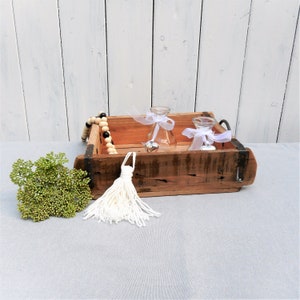 Könnte beinhalten: Ein Holztablett mit Metallgriffen, mit einem weißen Quasten, einer Schnur aus Holz- und schwarzen Perlen und zwei Glasvasen mit weißen Bändern.