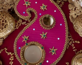 Puede incluir: Una bandeja decorativa de color rosa en forma de paisley con ribetes dorados y detalles de estrellas verdes. La bandeja tiene dos recortes circulares, uno más grande que el otro, que se pueden utilizar para velas u otros artículos decorativos.