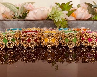May include: A row of eight tealight candle holders with gold trim and rhinestones. The candle holders are in various colors, including red, yellow, green, and pink.