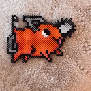 May include: A pixel art figure made of orange, black, white, and pink plastic beads. The design depicts a creature with a chainsaw blade protruding from its head and a tail shaped like a chainsaw starter handle, outlined in black beads.