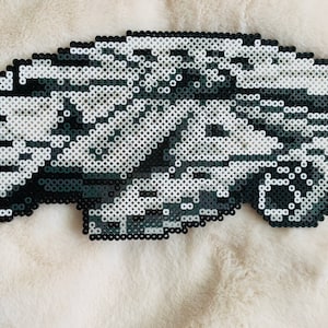 Op de afbeelding: Een zwart-wit pixel art ontwerp van een ruimteschip, gemaakt met kleine plastic kralen.