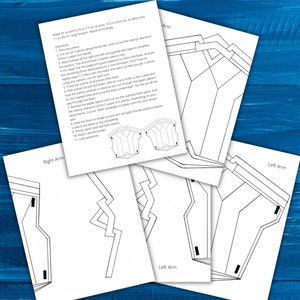 Puede incluir: Un montón de hojas de papel blanco con dibujos lineales negros para una armadura de brazo, incluyendo instrucciones y diagramas. El texto incluye medidas de 17 cm en la muñeca, 26,5 cm en el codo y 28 cm en el antebrazo. Sobre una superficie de madera azul.