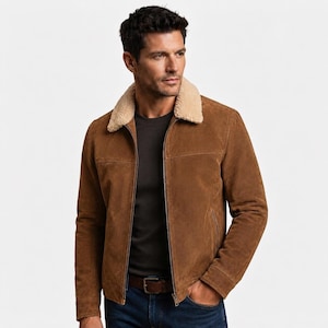 May include: A brown suede jacket featuring a beige shearling collar, a full-length front zipper closure, and horizontal seam detailing across the chest. The jacket is worn over a dark gray shirt and dark blue denim jeans with a brown leather belt.