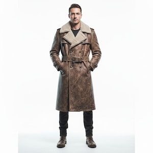 May include: A brown leather trench coat with a shearling collar and a belted waist. The coat has a double-breasted design and is knee-length. The model is wearing black trousers and brown boots.