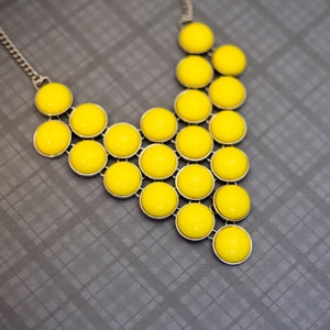 May include: A yellow statement necklace with a silver chain and round yellow beads arranged in a V-shape.