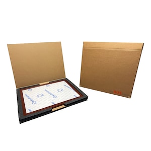 May include: A brown cardboard box with a flap open, revealing a brown wooden frame with a white backing. The frame is surrounded by black foam padding. The box is labeled "the BOX large".
