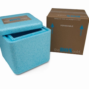 May include: A blue styrofoam cooler with the logo "the box cold." printed on the lid. The cooler is open and the lid is propped up. The cooler is sitting on a white surface. A brown cardboard box with the same logo is in the background. The box has the words "Saving our world one package at a time" and "PERISHABLE" printed on it.