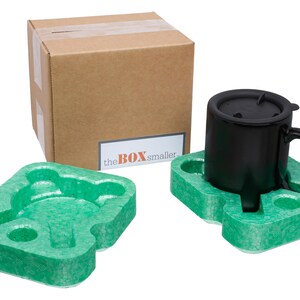 May include: A black mug with a black lid sits inside a green molded foam insert, with a matching empty green foam insert nearby. A brown cardboard box with a white label featuring the text "the BOX smaller" is positioned behind the mug.
