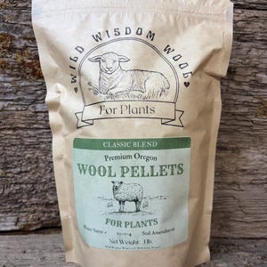 May include: A tan paper bag of "Wild Wisdom Wool" wool pellets for plants. The bag features a green label with text and a sheep illustration. The bag's net weight is 1 lb.